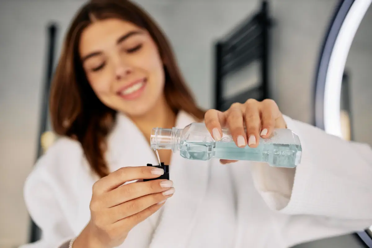 Close-up of a person rinsing their mouth with mouthwash in a bright bathroom setting, representing daily oral care and dental hygiene.