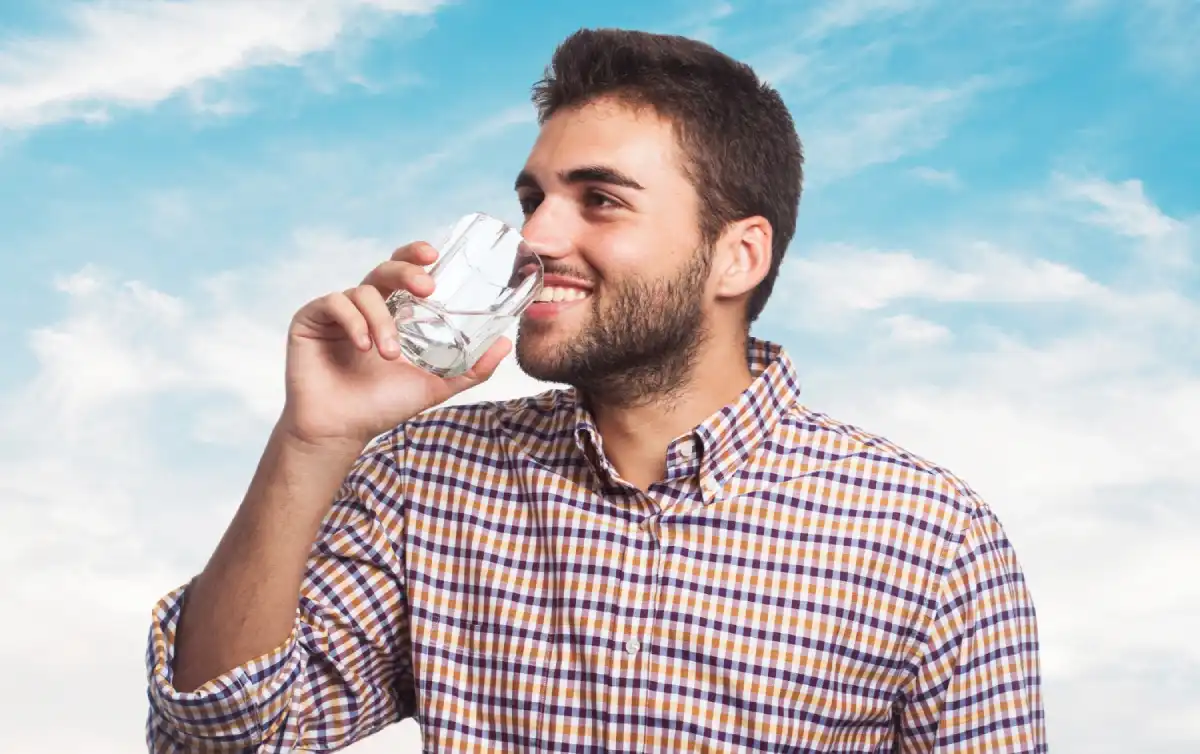 Smiling woman is drinking a glass of water, representing the dental benefits of staying hydrated for healthier teeth and gums.