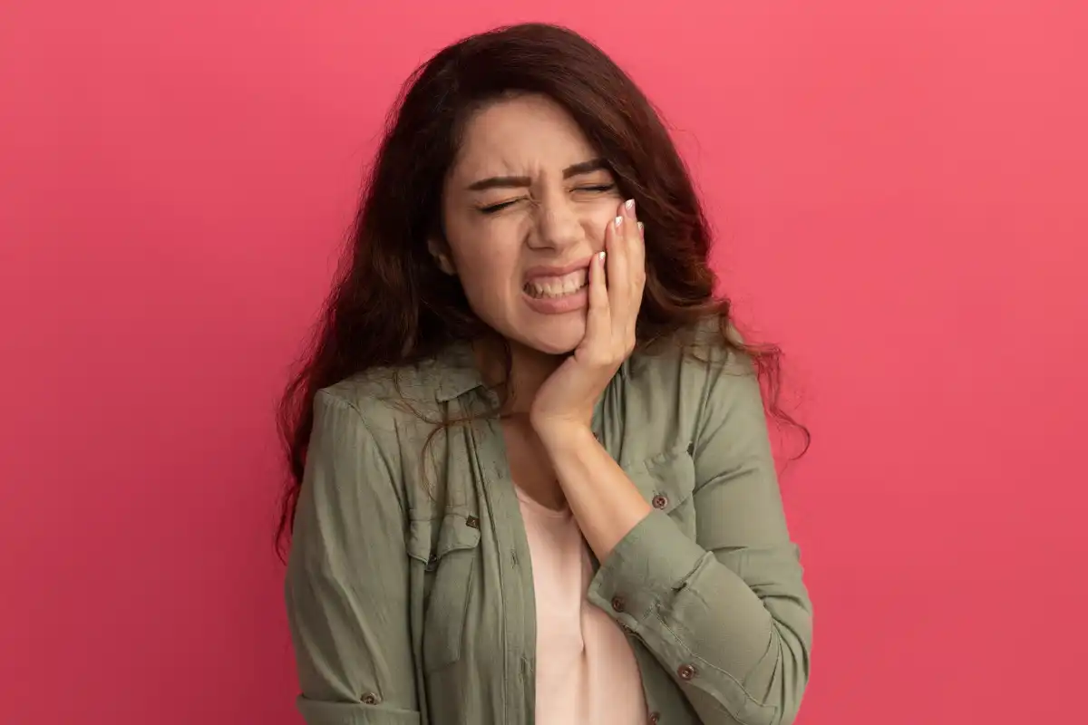 aching-young-beautiful-girl-wearing-olive-green-t-shirt-putting-hand-aching-tooth-isolated-pink-wall Woman holding her jaw and experiencing toothache or jaw pain, illustrating symptoms of dental discomfort, TMJ disorder, or oral health issues.